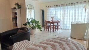 Una sala de estar con sofá, una mesa de centro, una mesa de comedor con sillas, una planta en maceta y una estantería.