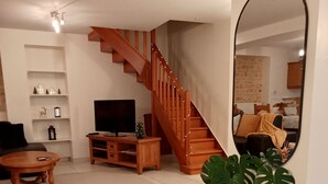 Una sala de estar con una escalera de madera, un televisor, una mesa de centro y una mesa de comedor con velas.
