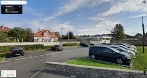 A parking lot with several cars, a building with a red roof, and a sign indicating a location in Luc-sur-Mer. - Spacious house 300 m from the sea. Sheltered garden (Luc-sur-Mer)