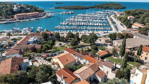 Una marina con numerose imbarcazioni ormeggiate, circondata da edifici residenziali con tetti in tegole rosse.