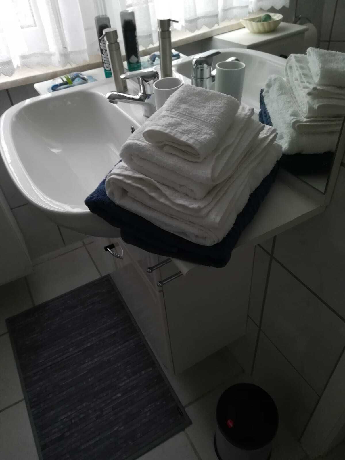 A bathroom with a white sink, a mirror, and a stack of white towels on a blue mat.