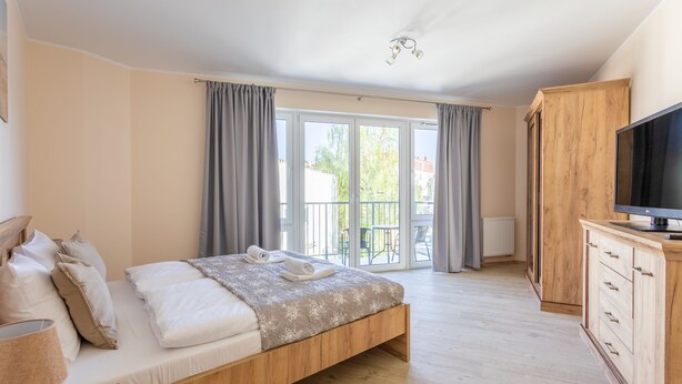 A bedroom with a wooden bed, a TV on a wooden cabinet, and a balcony with curtains. - Ferienwohnung am Meer, Urlaub auf der Insel Usedom, Appartement Centrum (Swinoujscie)