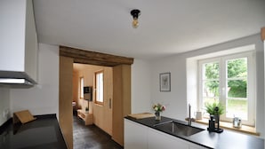 A modern kitchen with a black countertop, white cabinets, and a window with a view of greenery. - Ferienhaus Baustert (Baustert)