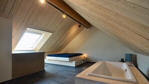 A modern attic bedroom with a skylight, a built-in bed, a bathtub, and a sloped ceiling. - Ferienhaus Baustert (Baustert)