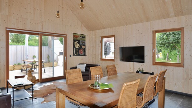 A spacious dining area with a large wooden table, wicker chairs, and a modern TV. - Ferienhaus Baustert (Baustert)