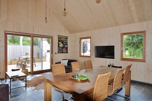 Ett rymligt matområde med ett stort träbord, flätade stolar och en modern TV.