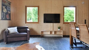 A modern living room with a leather sofa, a flat-screen TV mounted on the wall, a dining table with chairs, and a wooden ceiling. - Ferienhaus Baustert (Baustert)
