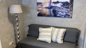 Um quarto aconchegante com um sofá cinzento, uma luminária e um quadro de uma paisagem rochosa.