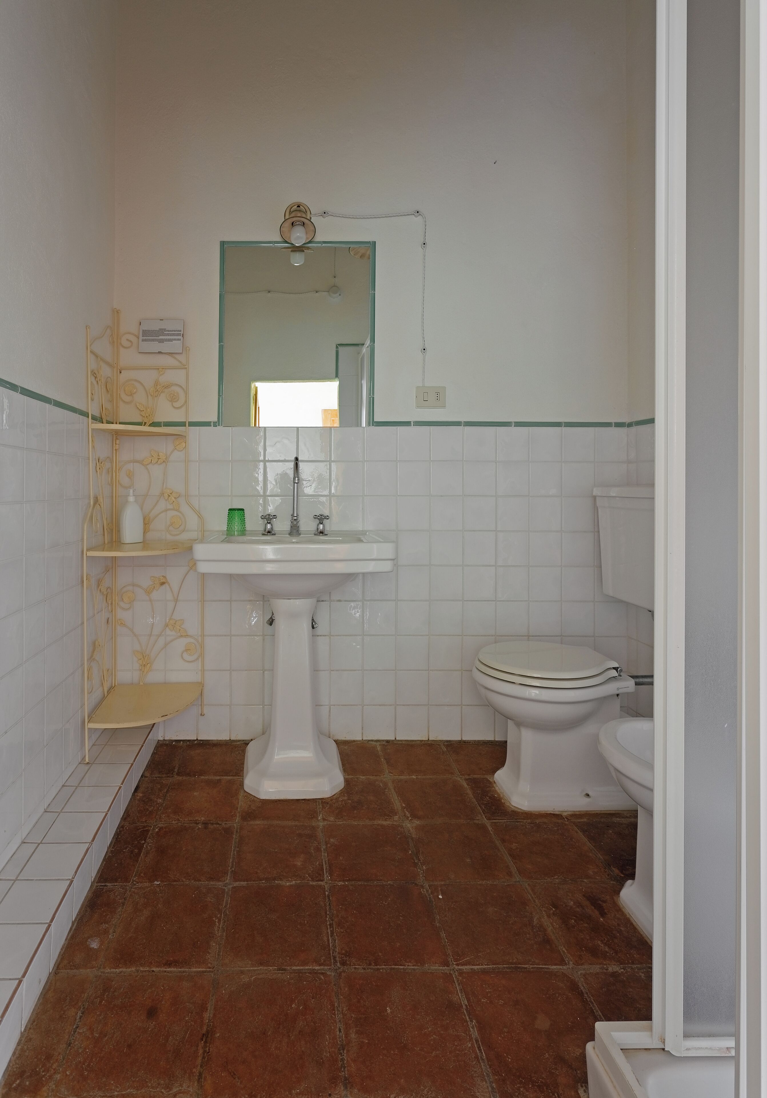 Une salle de bain avec un lavabo sur colonne, des toilettes et une étagère décorative.
