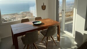 Ein Essbereich mit einem Holztisch, zwei Stühlen und Meerblick durch große Fenster.