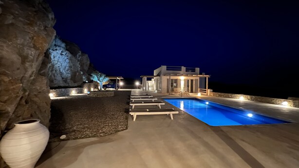 Eine moderne Villa mit Swimmingpool, Sitzgelegenheiten im Freien und Blick aufs Meer bei Nacht.