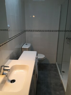 Un baño pequeño con lavamanos, inodoro y ducha con mampara de vidrio.