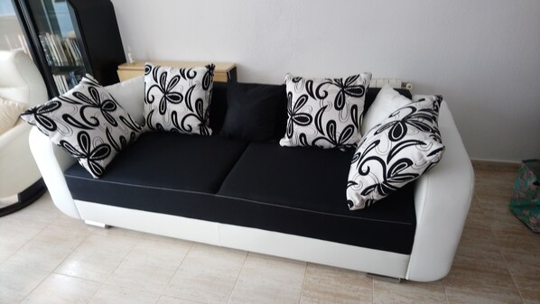 A modern sofa with black and white patterned cushions, a wooden side table, and a tiled floor.