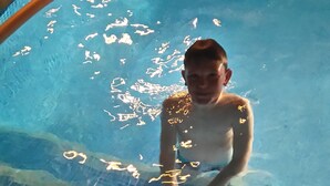 Una persona en una piscina amb aigua blava cristal·lina i vores de rajola.