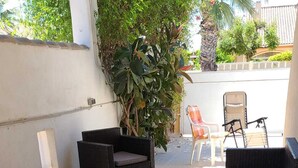 Zona de pati amb mobiliari de vimet, sòl de rajola i una planta en test.