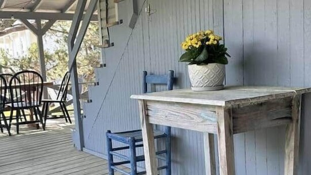 A wooden deck with a table and chairs, a potted plant, and a rustic wall.