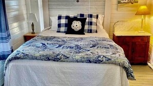 A bedroom with a bed, a nightstand, a lamp, a window with curtains, and a painting on the wall.