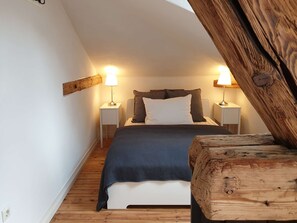 Un dormitorio con techo inclinado, una cama con manta azul, dos lámparas de noche y un cabecero de madera.