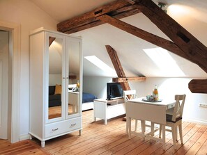 A room with a sloped ceiling, wooden beams, a white wardrobe, a desk with a chair, and a television. - Grombach Train Station - FUCHSBAU - a small, cozy apartment ideal for solo travelers (Bad Rappenau)