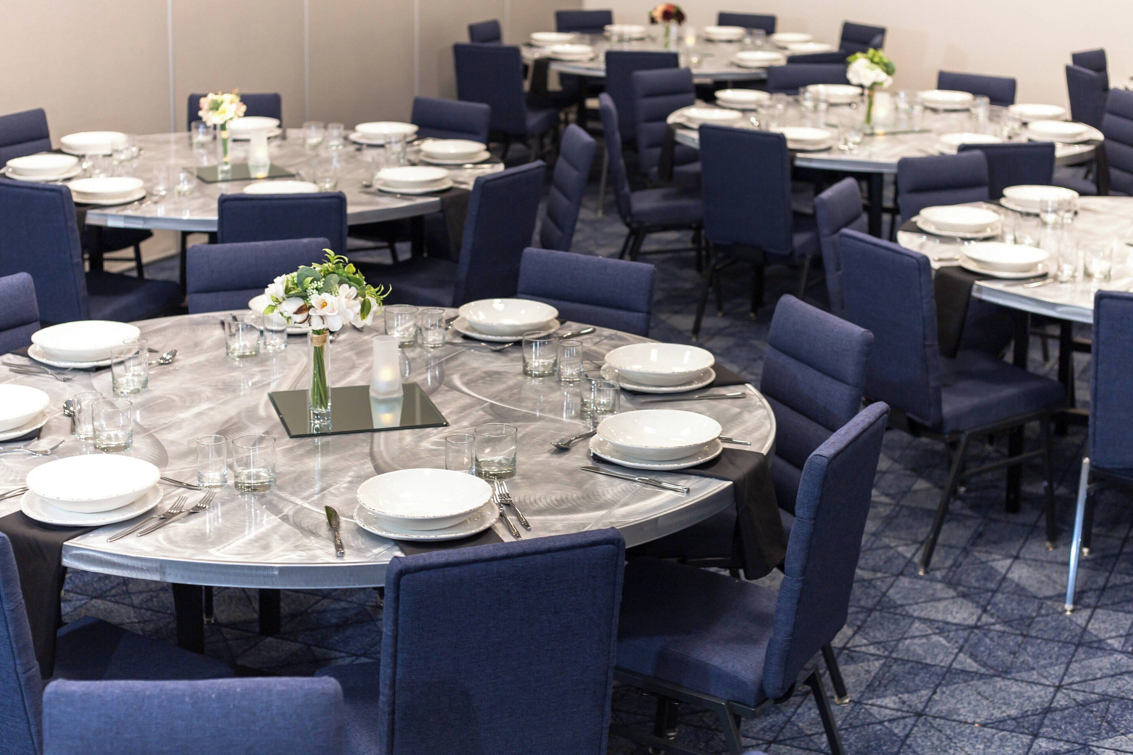 Une salle de conférence avec des tables rondes, des chaises bleues et des assiettes blanches, le tout préparé pour une réunion.