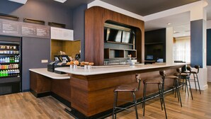 Eine moderne Bar mit Holztresen, Barhocker, einem Getränkespender und einer Speisekarte.