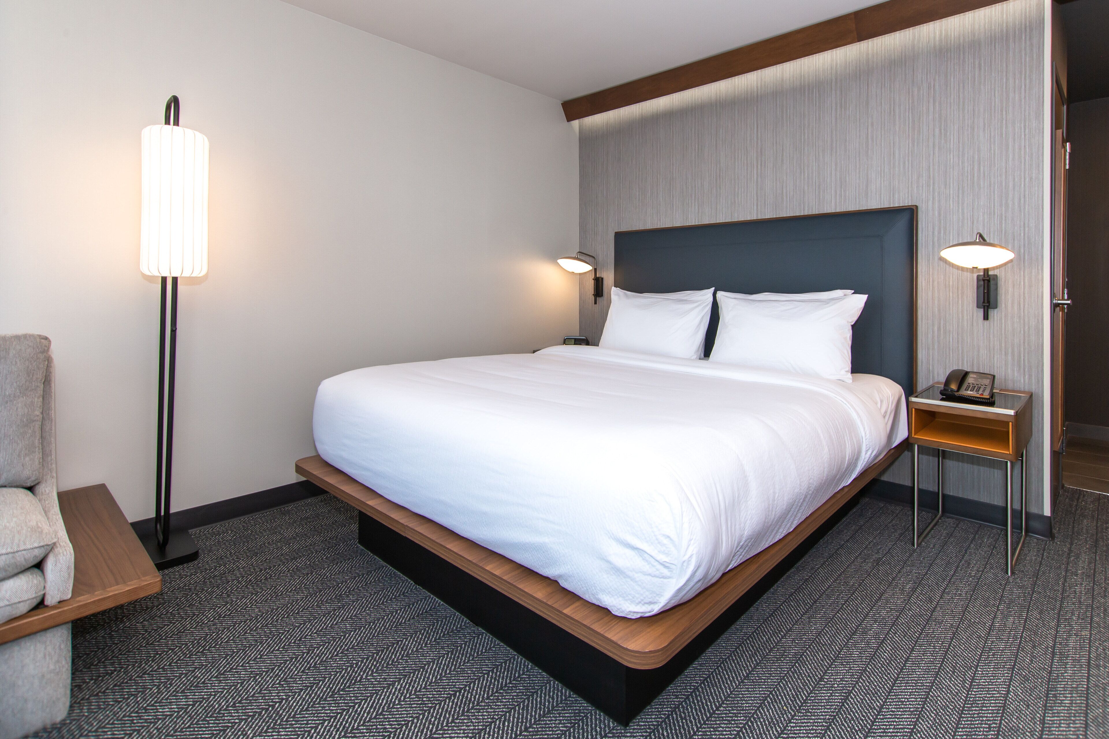 A hotel room with a large bed, two bedside tables, a chair, and a floor lamp.