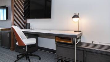 Una habitación de hotel moderna con escritorio, silla, televisor y lámpara.