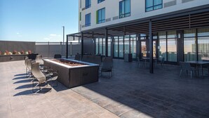 Eine Dachterrasse mit Außenmöbeln, einem Feuerkorb und einem modernen Gebäude im Hintergrund.