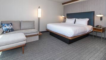Una habitación de hotel con cama, sofá, mesita de noche y lámpara de pie.