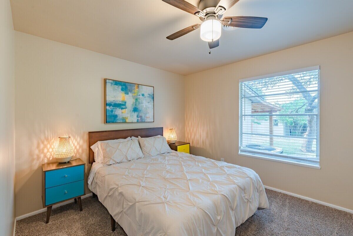 A bedroom with a bed, a ceiling fan, a window with blinds, and a painting on the wall.