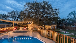 A backyard with a swimming pool, wooden deck, and outdoor seating area with string lights. - Private Pool, Game Room, Fire Pit & Huge Backyard near Six Flags (San Antonio)