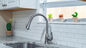 A kitchen with a stainless steel sink, white tiled backsplash, and potted plants on the windowsill. - Private Pool, Game Room, Fire Pit & Huge Backyard near Six Flags (San Antonio)