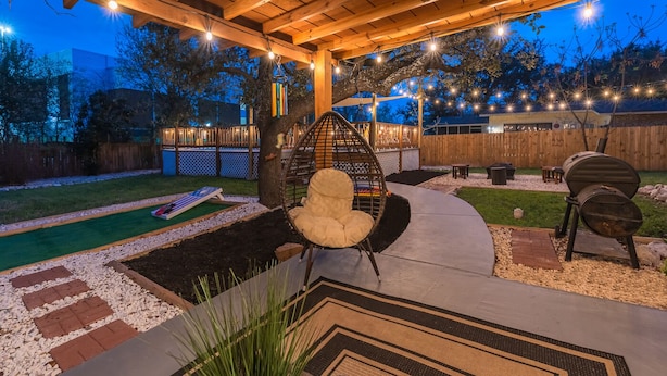 An outdoor patio area with a swing chair, a barbecue grill, and a small table. - Private Pool, Game Room, Fire Pit & Huge Backyard near Six Flags (San Antonio)