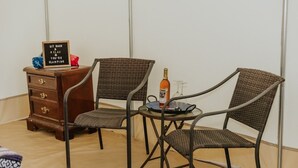 Una habitación con dos sillas de mimbre alrededor de una mesa pequeña, un aparador de madera con cajones y un cartel sobre el aparador.