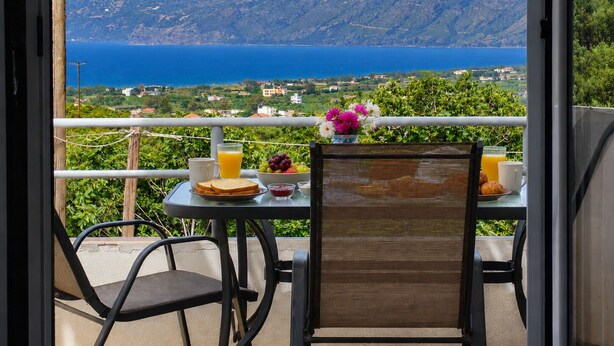 Ein Balkon mit Frühstückstisch, mit Blick auf eine reizvolle Landschaft aus Meer und Hügeln.