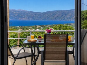 Un balcón con una mesa preparada para el desayuno, con vistas panorámicas al mar y las colinas.