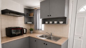 Eine kompakte Küche mit grauen Schränken, einem Einbauofen, einem Spülbecken und einem kleinen Fenster mit Vorhängen.