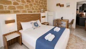 Ein Hotelzimmer mit Steinwand, einem Bett mit blauer Decke, einem Schreibtisch und einer Küchenzeile.