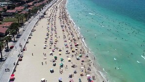 Uma praia com fileiras de guarda-sóis e pessoas.