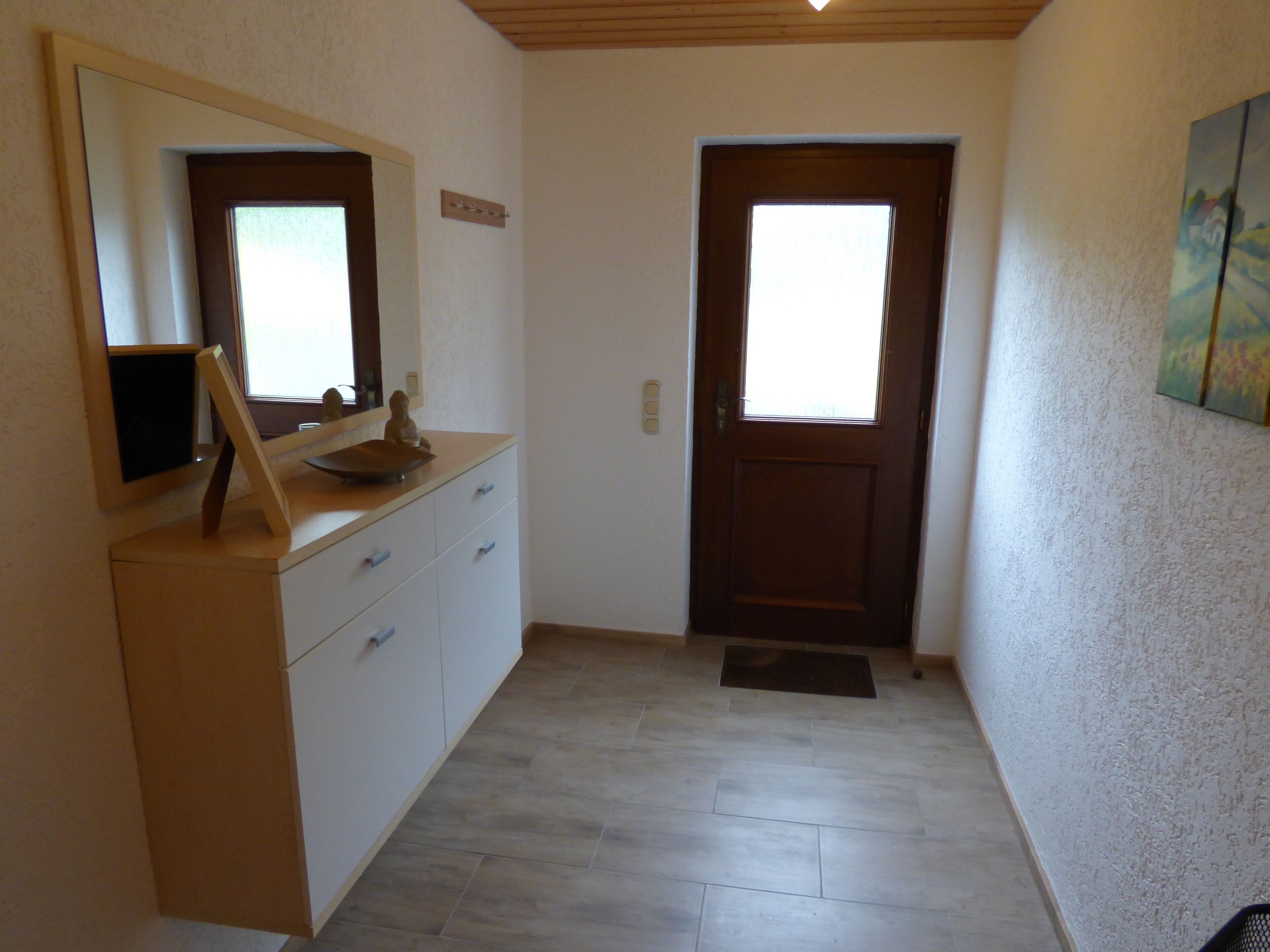 Un couloir avec une porte en bois, une commode blanche avec un miroir et une petite fenêtre.