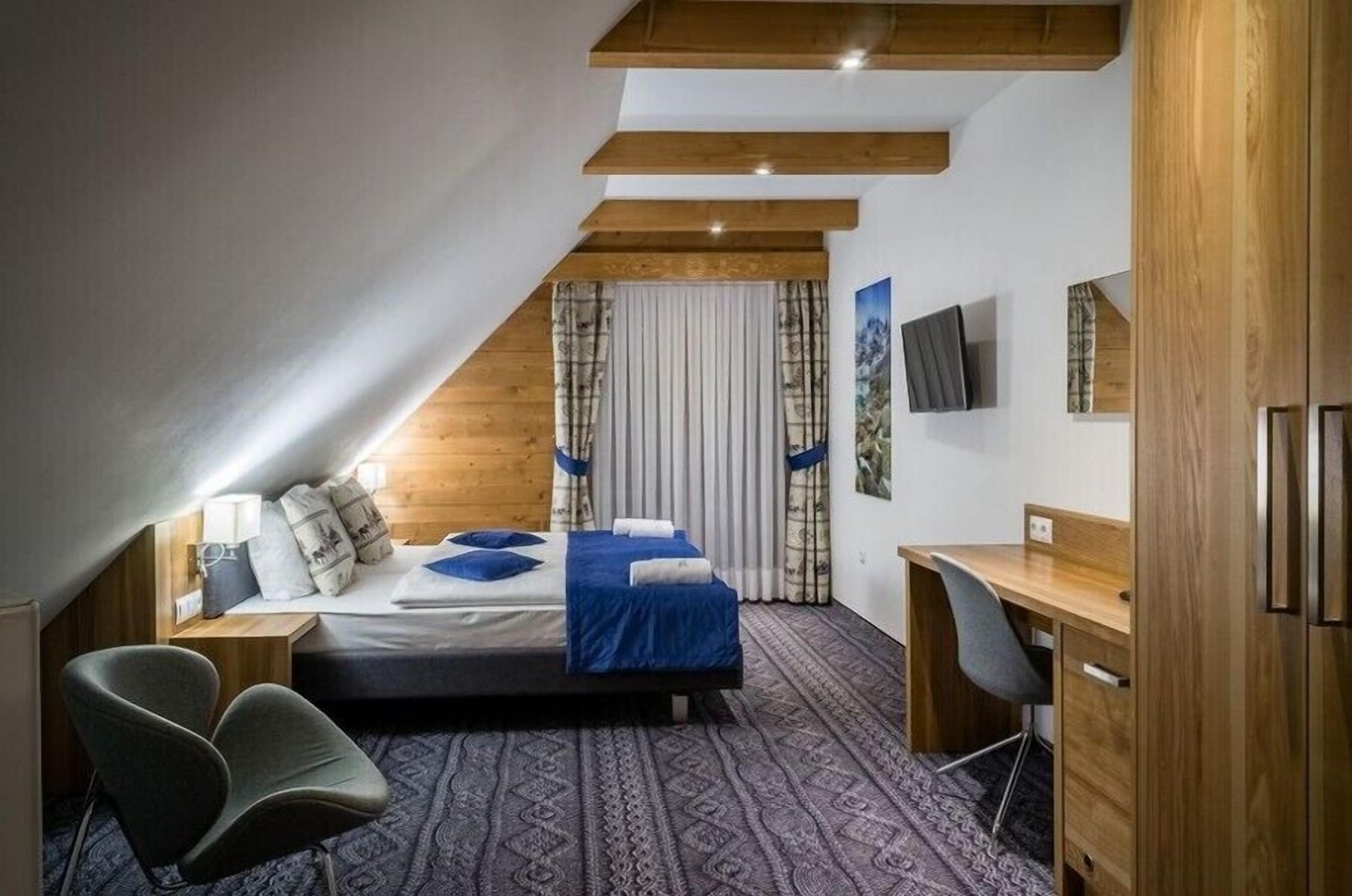 A bedroom with a sloped ceiling, a bed with blue bedding, a desk, and a chair.