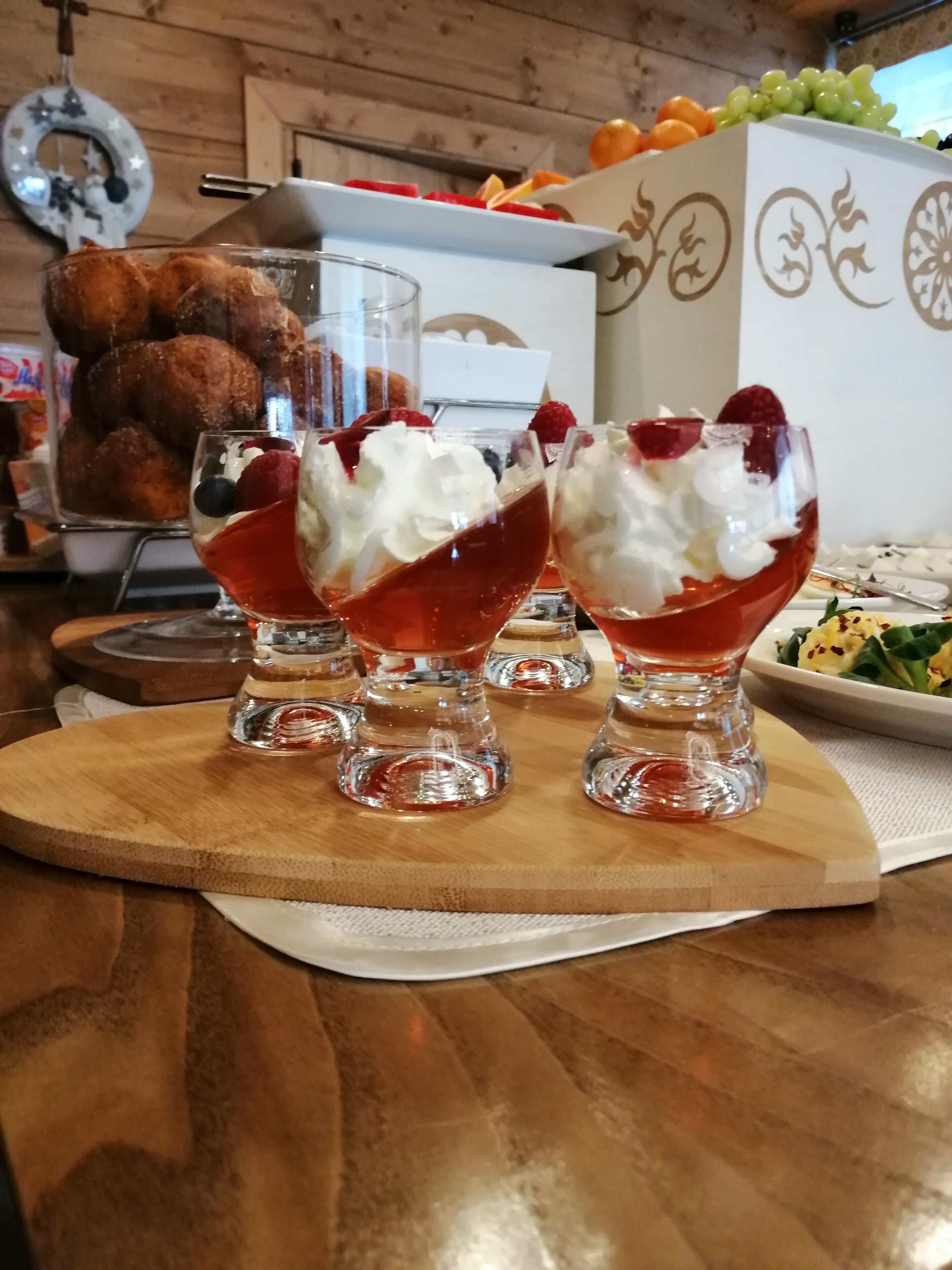 Three dessert glasses with whipped cream and berries on a wooden board.