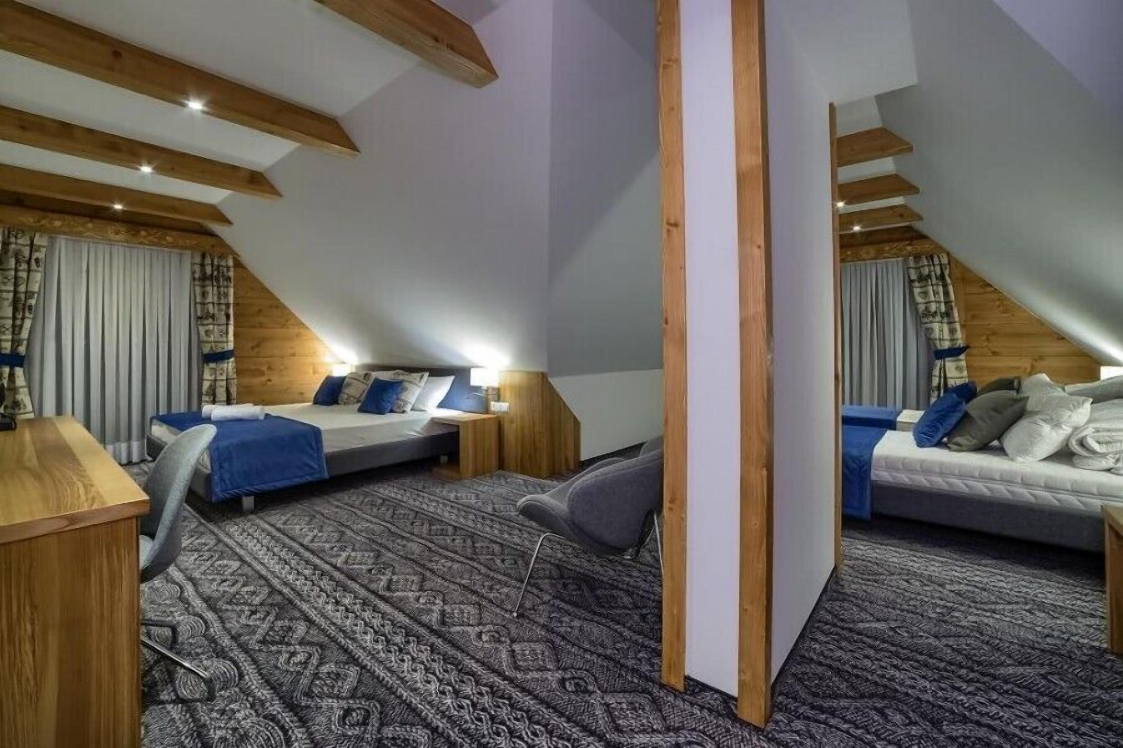 A bedroom with two beds, a desk, and a chair. The room has sloped ceilings and wooden beams.