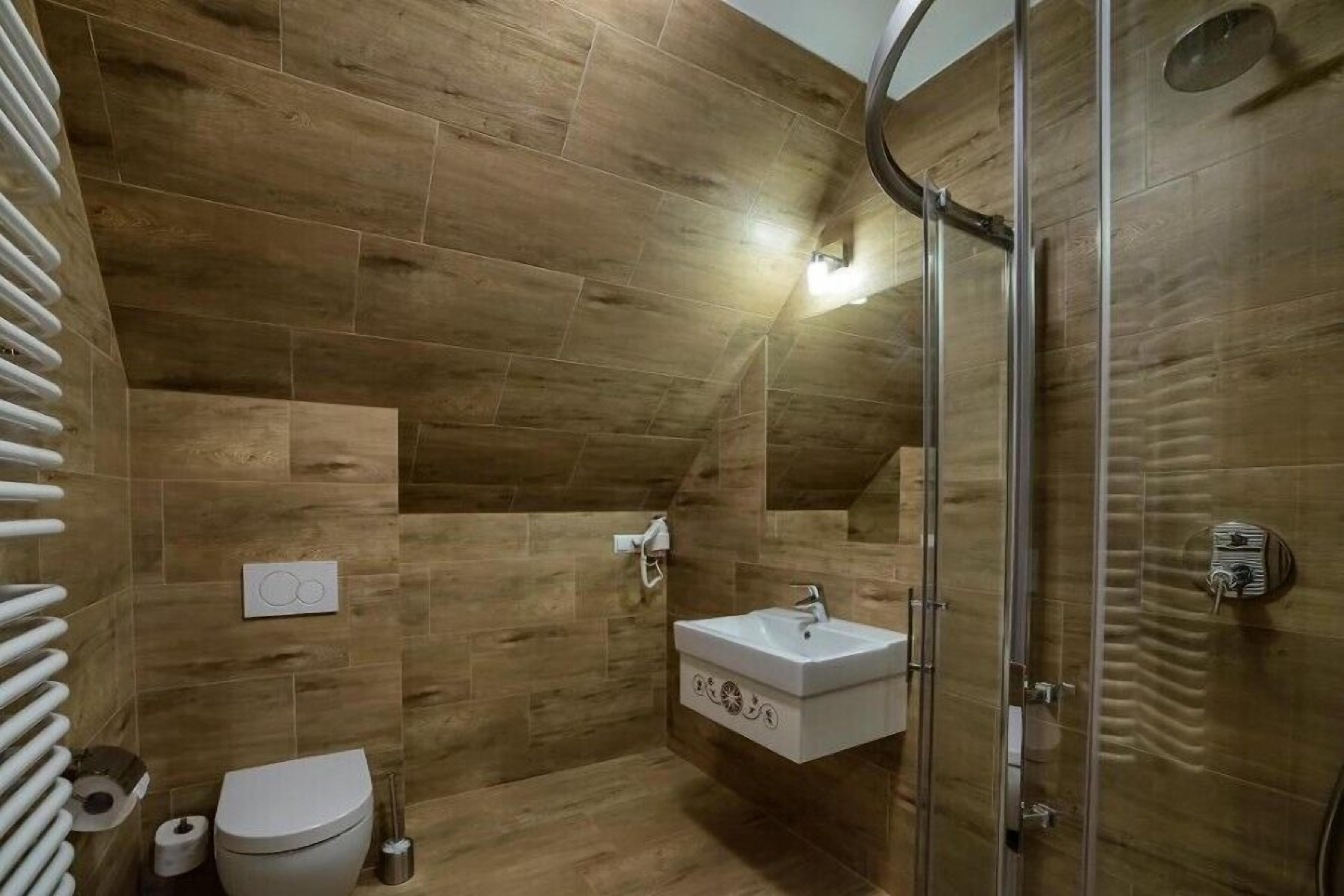 Un baño moderno con baldosas de madera, un inodoro, un lavamanos y una ducha.