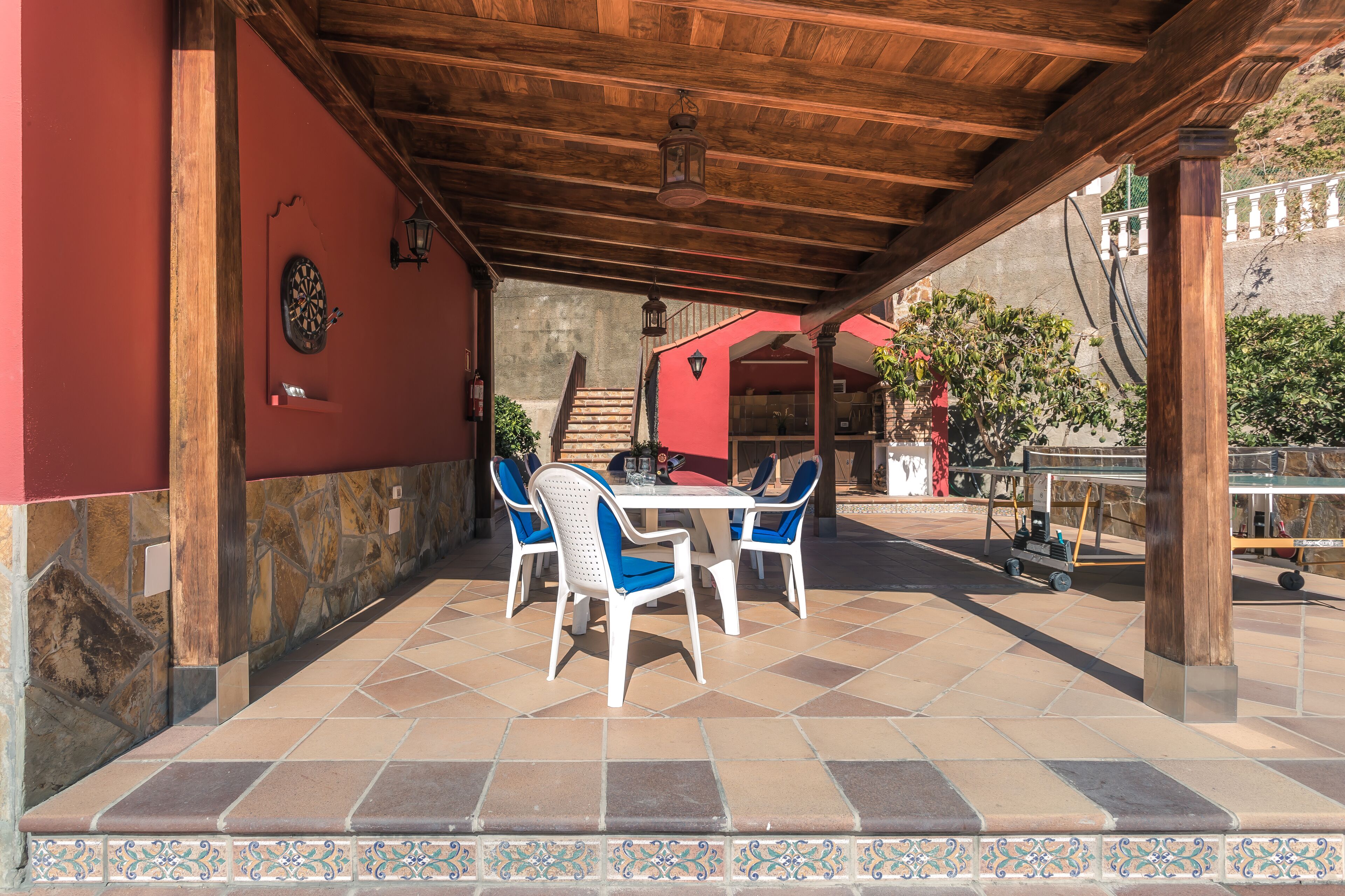 An outdoor patio with a wooden pergola, stone walls, and a table with chairs.