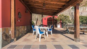 An outdoor patio with a wooden pergola, stone walls, and a table with chairs.