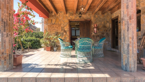 Un patio cubierto con paredes de piedra, techo de madera y mobiliario exterior.
