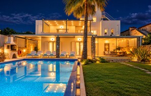 A modern two-story house with a swimming pool, outdoor seating, and a well-lit patio area.