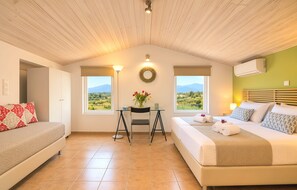 A bedroom with a bed, a desk, and two windows with a view of the countryside.