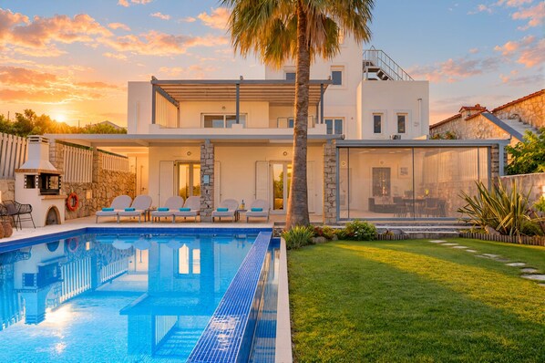 A modern two-story house with a swimming pool, outdoor seating, and a stone facade.